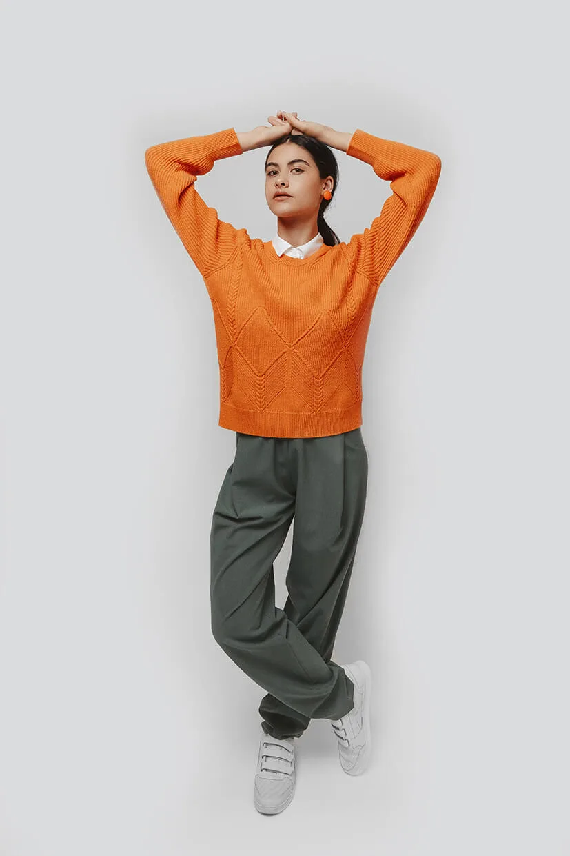 femme portant un pull orange en laine et un pantalon gris