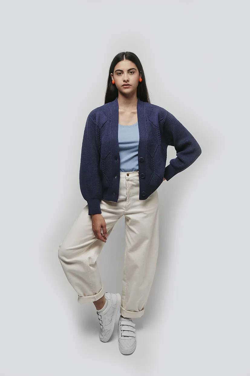 jeune femme brune portant un cardigan bleu et un pantalon blanc