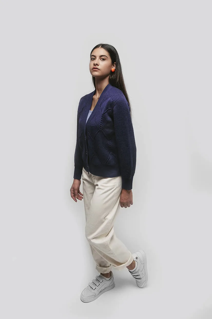 femme brune debout avec une veste bleu marine et un pantalon blanc