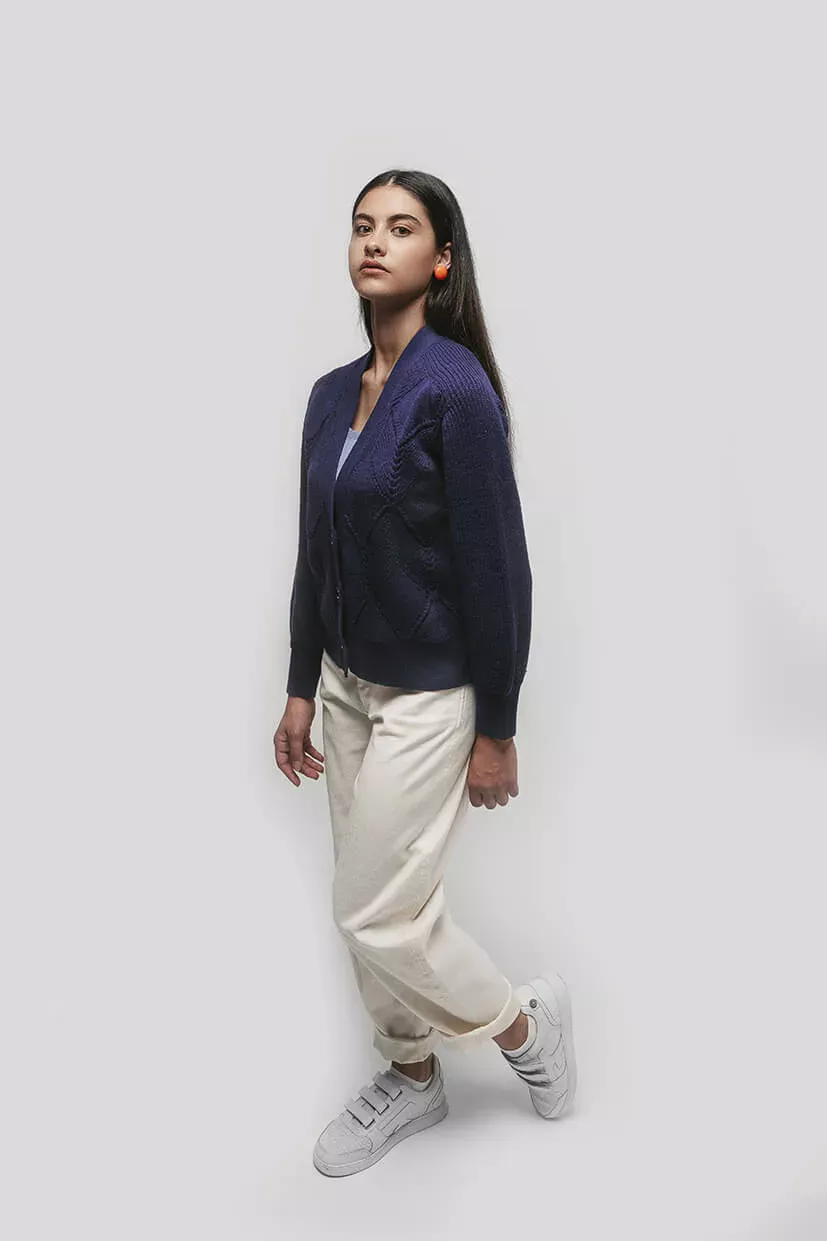 femme brune debout avec une veste bleu marine et un pantalon blanc